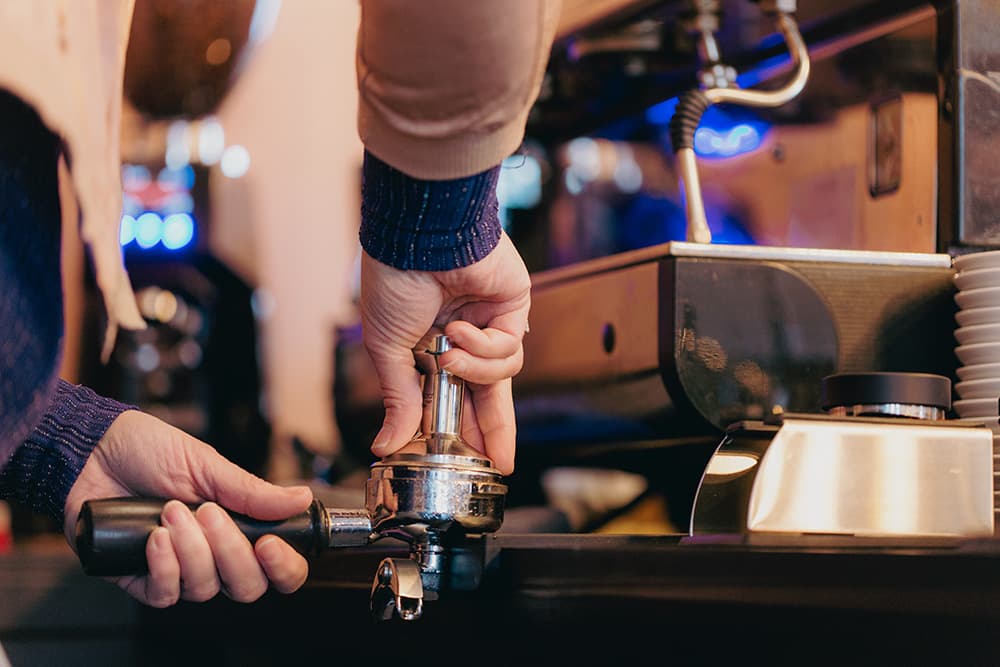 Handen die de koffie aandrukken in de filterhouder van de espressomachine