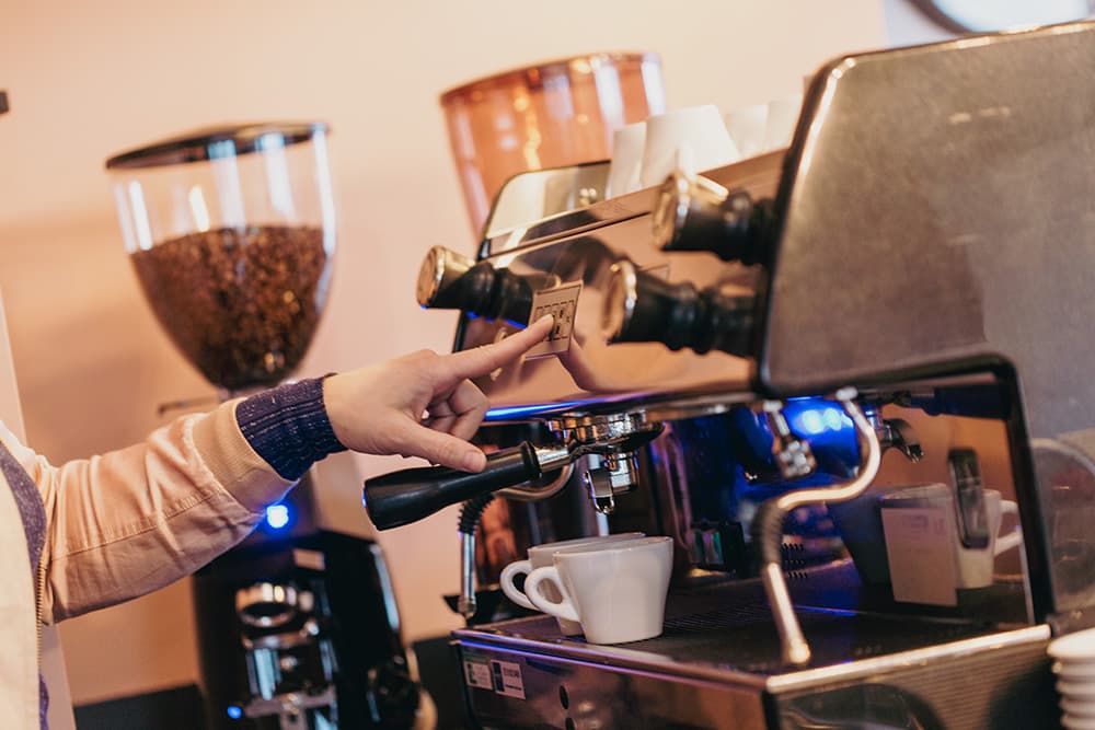 Een vrijwilliger zet koffie aan de espressomachine van De Blije Boon
